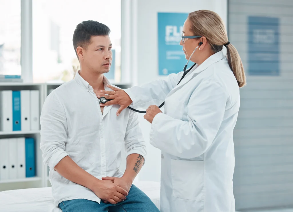 a female doctor checks the heart rhythm of a 20-something male patient with a stethoscope